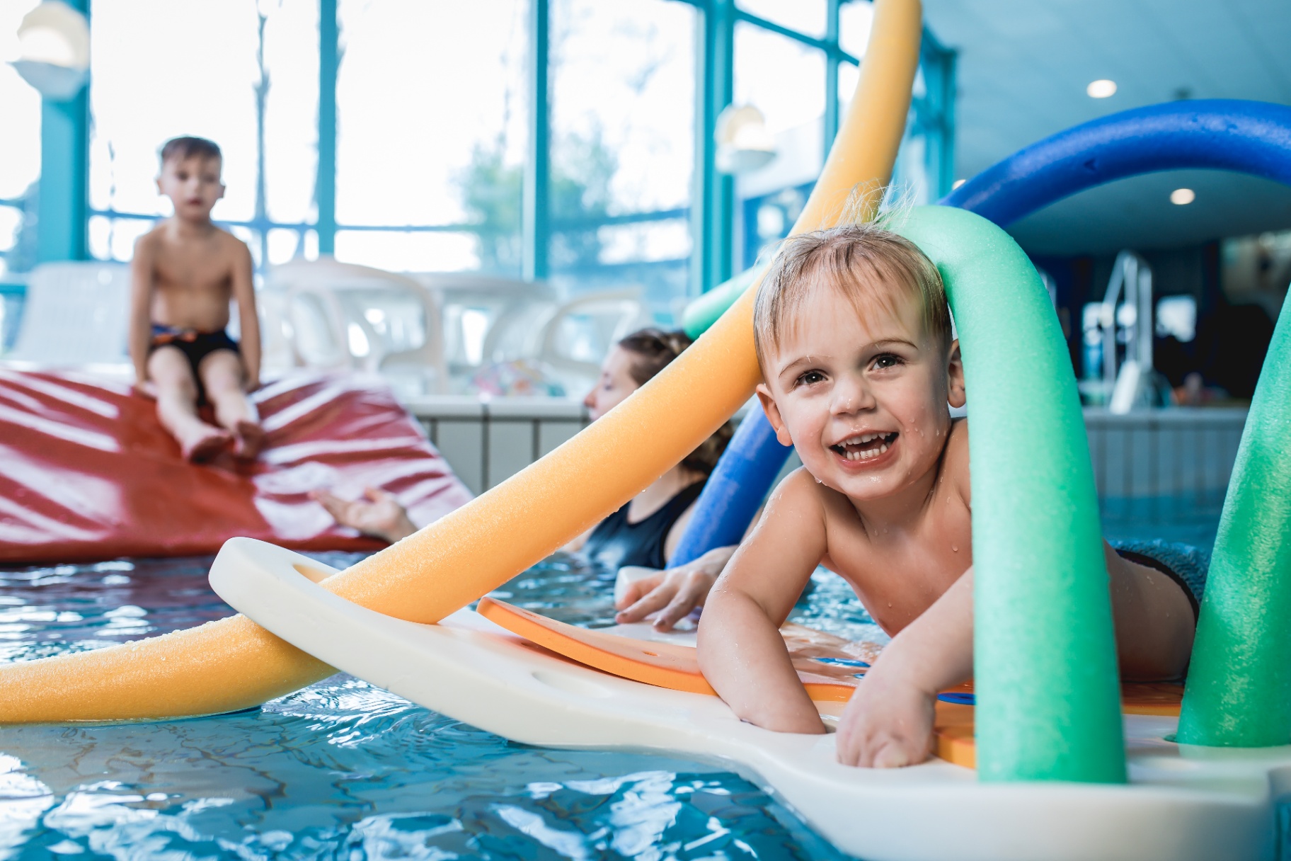 Lachende peuter speelt met drijvend materiaal tijdens Peuterzwemmen in het warme recreatiebad