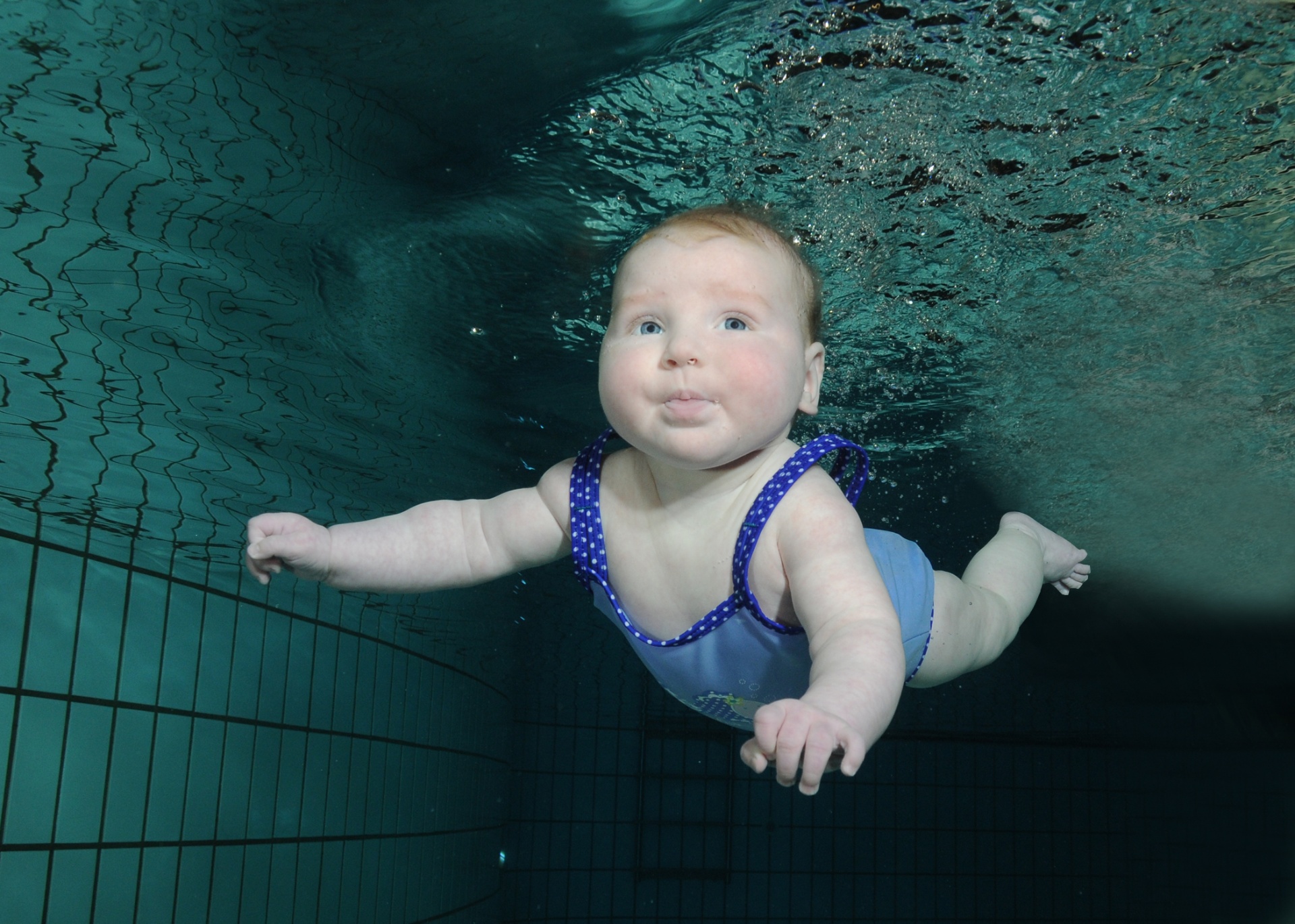 Baby met blauw badpakje beweegt onder water tijdens Baby- en Peuterzwemmen bij Zwembad De Meerval