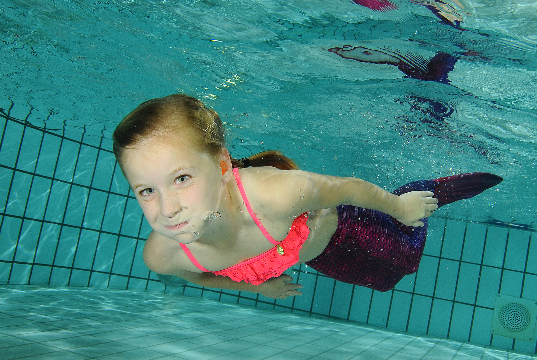 Kind zwemt onder water met paarse zeemeerminnenstaart in Zwembad De Meerval